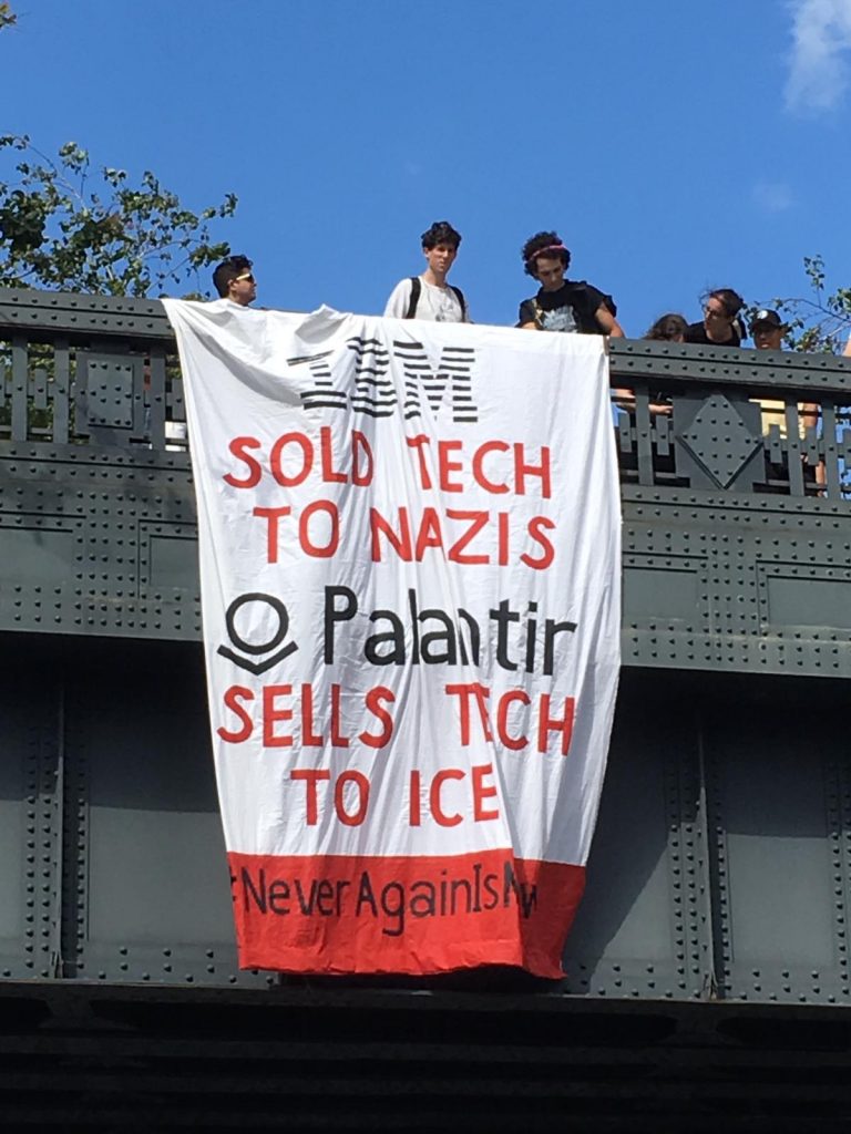 Image of banner drop painted with the words "IBM sold tech to Nazis; Palantir sells tech to ICE #NeverAgainISNow"